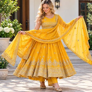 May include: A vibrant yellow Anarkali suit featuring a sleeveless bodice and a full, pleated skirt. The garment is adorned with intricate silver embroidery and sequin detailing along the hem and neckline, paired with a matching sheer dupatta.