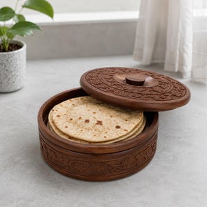 May include: A round, dark brown wooden container with a matching lid, featuring intricate floral carvings on the exterior and lid. Inside the container sits a stack of several round, flat, light brown unleavened flatbreads or tortillas.