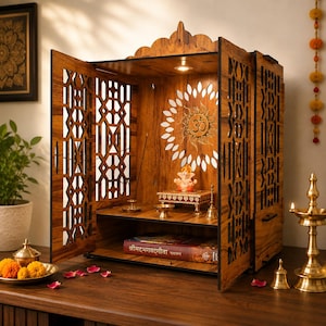 Può includere: Un tempio domestico in legno con intricati motivi geometrici tagliati al laser sulle porte e sui pannelli laterali. La parete interna mostra un simbolo Om dorato circondato da un design a raggiera. Una piccola statuetta di Ganesha è posata.