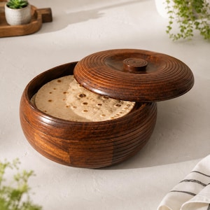 May include: A round, dark brown wooden container with a matching lid, featuring horizontal grooved lines along the exterior sides and the top of the lid. The container is partially open, revealing several flat, round, beige flatbreads inside.
