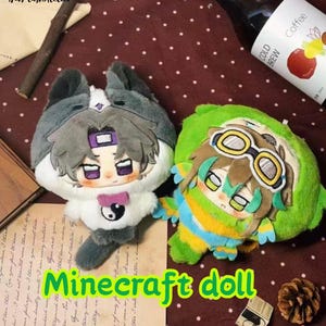May include: Two plush dolls featuring stylized anime-inspired faces. The left doll has gray and white fur, a purple headband, and a yin-yang symbol on its chest. The right doll is green with brown hair, wearing yellow and white goggles.