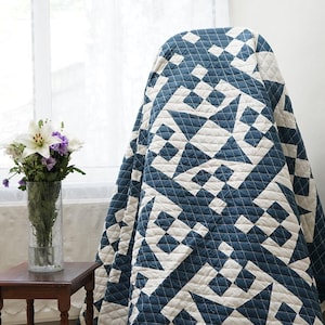 Op de afbeelding: Een quilt met een geometrisch patroon in diepblauw en gebroken wit. De stof toont een herhalend ontwerp van onderling verbonden vierkanten en stervormige figuren met zichtbare rasterstiksels over het gehele oppervlak van het textiel.