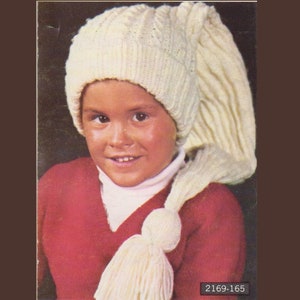 Puede incluir: Un niño con un gorro de punto color crema con una cola larga y puntiaguda y una borla. El sombrero se combina con un suéter rojo. La imagen tiene una estética vintage.