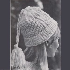 May include: A white knitted hat with a long, dangling tassel. The hat has a cable knit pattern and a slouchy fit.