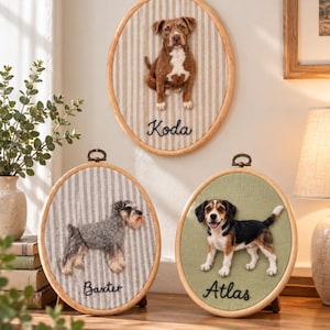 May include: Three oval wooden embroidery hoops featuring needle-felted dog portraits. One hoop displays a brown and white dog named Koda on striped fabric, another a grey schnauzer named Baxter on striped fabric, and a beagle named Atlas on green fabric.