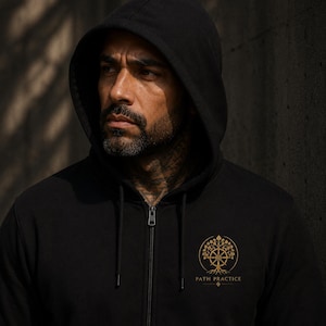 May include: A black zip-up hoodie featuring a gold-colored circular graphic on the left chest. The design depicts a stylized tree with roots and a central wheel element, with the text "PATH PRACTICE" printed in gold lettering directly below the icon.