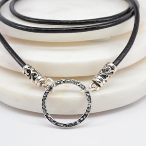 May include: A black leather cord necklace with silver-toned metal accents and a hammered circle pendant.