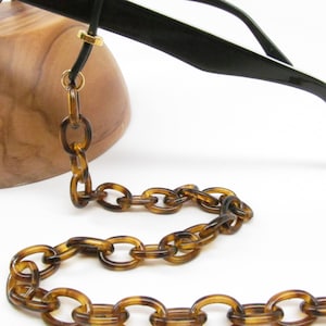 May include: A tortoiseshell plastic chain for glasses. The chain is made of oval links and has gold-tone metal clasps.