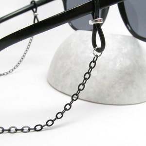 May include: Black sunglasses with a black chain attached to the arms. The chain is made of small, linked metal circles.