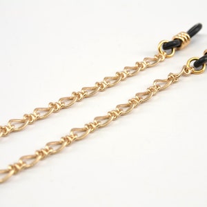 May include: A pair of gold-tone eyeglass chains with black rubber ends. The chains are made of a delicate, linked design.