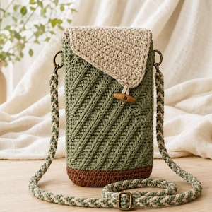May include: A vertical crochet crossbody bag featuring a sage green body with a diagonal ribbed texture, a beige flap, and a dark brown base. The bag includes a wooden toggle closure, bronze-toned metal hardware, and a braided strap in beige and sage green.