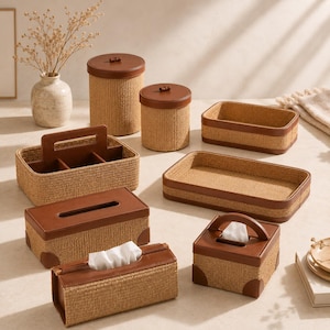 May include: A collection of storage organisers featuring woven tan natural fibre bodies and smooth brown leather trim. The set includes cylindrical canisters, rectangular trays, a handled caddy, and tissue box covers with white tissues visible.