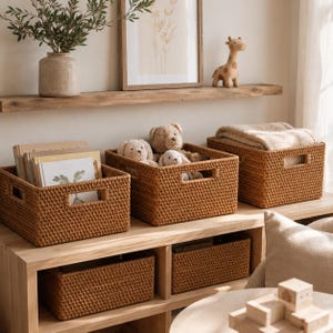 May include: Five rectangular woven storage baskets with integrated handles. Three baskets sit on a wooden shelf, holding books, plush toys, and a folded blanket. Two additional matching baskets are placed in the lower storage cubbies.