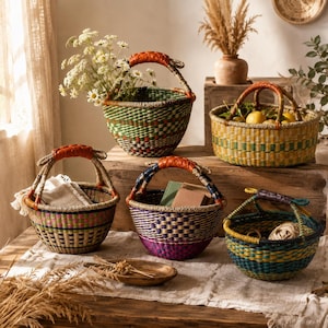 May include: Five woven baskets with leather-wrapped handles in various sizes and colors. The baskets feature intricate patterns in green, yellow, purple, and blue, with some containing white flowers, lemons, books, and twine on a wooden surface.