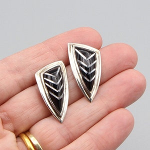May include: A pair of silver earrings with black onyx stones in a geometric arrow shape.