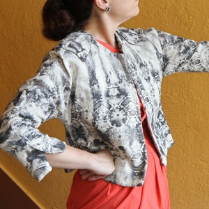 May include: A patterned jacket with a snakeskin design in black and white. The jacket is open in the front, revealing a red top underneath. The sleeves are three-quarter length.