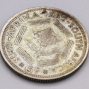 May include: A silver South Africa coin from 1952. The coin features the text "SUID-AFRIKA" and "SOUTH AFRICA" around the edge. The center design includes a floral element and the denomination "6D".