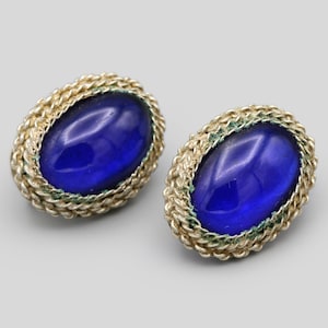 May include: A pair of oval-shaped stud earrings. Each earring features a vibrant blue, oval-shaped stone set within a gold-colored, rope-like border. The earrings are displayed on a light gray background.