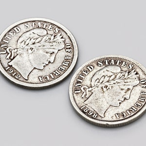 May include: Two silver Barber dimes from the United States. The coins are circular with a profile of a woman wearing a laurel wreath. The text "UNITED STATES OF AMERICA" and the year are visible. One coin is dated 1912, the other 1898.