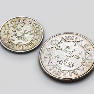 May include: Two silver coins with Arabic script on both sides. The coins are slightly worn and have a patina.