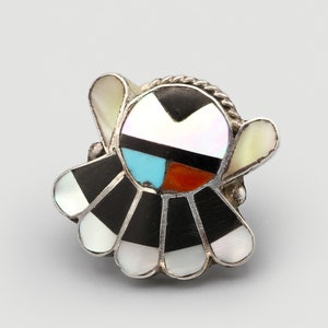 May include: A silver ring with a colorful inlaid design. The ring features a central circular design with black, white, turquoise, and red segments, surrounded by fan-shaped black and white sections. Two curved white sections flank the central design.