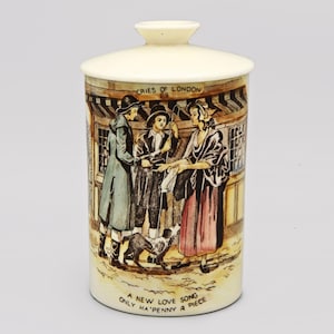 May include: A cream-colored ceramic jar with a lid, featuring a detailed illustration of a street scene with figures in period clothing. The text "Cries of London" and "A new love song only ha'penny a piece" are visible.
