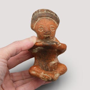 Escultura artesanal em terracota representando uma figura sentada, estilo arte popular pré-colombiano, estilo Colima, México Ocidental.