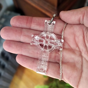 Op de afbeelding: Een hanger in de vorm van een Keltisch kruis van helder kristal aan een zilveren ketting. Het kruis is versierd met ingewikkelde ontwerpen en is een prachtig sieraad.