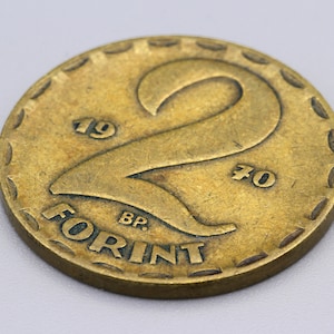 May include: A vintage gold-colored coin with the number "2" prominently displayed. The coin features the text "FORINT" and the years "1970" and "1970". The coin has a textured edge.