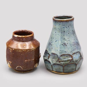 Puede incluir: Dos jarrones de cerámica, uno marrón con un esmalte moteado y el otro azul con un esmalte moteado y un diseño texturizado.