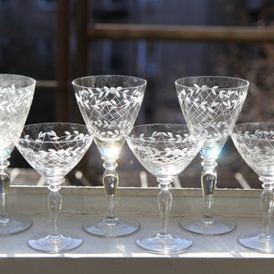 Pode incluir: Conjunto de seis taças de vinho transparentes com desenhos florais e treliçados gravados. As taças variam em tamanho, algumas têm uma forma cónica mais alta e outras uma taça mais curta e arredondada. Estão dispostas numa janela.
