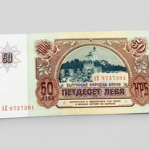 May include: A vintage Bulgarian 50 leva banknote featuring a red and brown design with a building in the center. The text "БЪЛГАРСКЯ НАРОДНА БАНКА" and "ПЕТДЕСЕТ ЛЕВА" is printed on the banknote.
