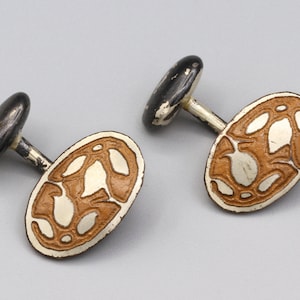 Könnte beinhalten: Ein Paar silberne Manschettenknöpfe mit braunem Emaille-Design. Die Manschettenknöpfe sind oval geformt und haben eine schwarze Metallrückseite.