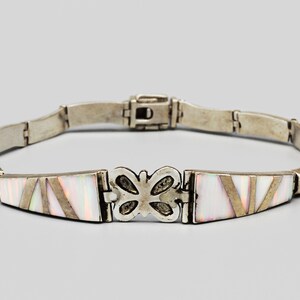 May include: Silver bracelet featuring rectangular opal inlays with diagonal silver accents. The bracelet includes a butterfly-shaped centerpiece and a secure clasp. A delicate piece of jewelry.