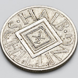 May include: A silver coin with the words "HALB SCHILLING" and the number "1/2" inside a diamond shape. The coin has a worn appearance and is set against a gray background. The numbers 2, 6, 9, and 5 are also visible on the coin.