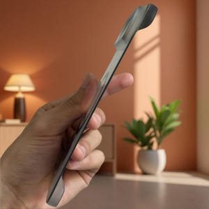 Puede incluir: Un tirador fino y alargado de color gris oscuro con un perfil curvo y ergonómico. El objeto presenta un acabado liso y mate con una sección superior ligeramente ensanchada, diseñado para su fijación en muebles o armarios con estilo.