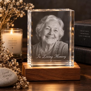 May include: A rectangular clear glass block featuring a laser-etched portrait of an elderly person with the text In Loving Memory and a small heart symbol. The glass block sits on a rectangular wooden base that illuminates the crystal from below.