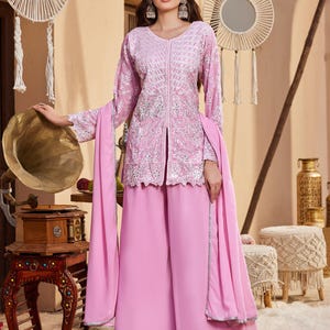 Könnte beinhalten: Eine hellrosa langärmelige Tunika mit aufwendiger weißer Blumenstickerei und einem Schlitz in der vorderen Mitte, kombiniert mit einer passenden weiten Hose und einem einfarbigen hellrosa Dupatta. Der Saum der Tunika und die Hosenbeine sind bestickt.