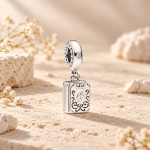 Puede incluir: Un charm de plata con un colgante rectangular grabado con la cabeza de un caballo, una pequeña corona y volutas. La anilla superior está decorada con un borde de cuentas y una pequeña piedra clara engastada en el centro.