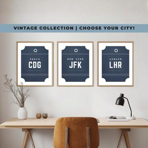 May include: Three framed wall art prints featuring dark blue luggage tag designs with white text. The prints display airport codes for Paris CDG, New York JFK, and London LHR, each with city names and coordinates in a clean, sans-serif typeface.