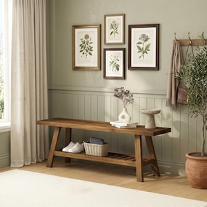 May include: A rectangular wooden bench with a lower slatted shelf, featuring a light brown finish. The bench holds a white ceramic vase with dried flowers, a stack of two white books, and a small stone pedestal bowl. A woven basket sits below.