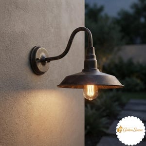May include: A dark, weathered metal wall sconce featuring a curved arm and a wide, downward-facing shade. The fixture holds a single exposed Edison-style light bulb that emits a warm glow, illuminating the textured wall surface behind it.