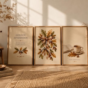 Könnte beinhalten: Drei gerahmte Wandbilder mit herbstlichen Motiven. Das linke Bild zeigt Eichenblätter und Eicheln mit dem Text "GOLDEN AFTERNOON". Das mittlere Bild zeigt einen Strauß aus Eichenblättern, der mit einem Band zusammengebunden ist. Das rechte Bild zeigt eine Kaffeetasse, ein offenes Buch und Eichenblätter mit dem Text "SLOW MORNINGS".