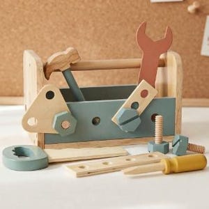Puede incluir: Una caja de herramientas de juguete de madera natural y azul apagado, que contiene un martillo, una llave inglesa y varias piezas de construcción de madera, incluyendo pernos, tuercas y un destornillador de mango amarillo, sobre una superficie plana.