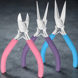 May include: A set of three metal pliers featuring silver-toned heads and ergonomic handles in solid pink, purple, and light blue. The collection includes a pair of wire cutters, round-nose pliers, and needle-nose pliers for precision tasks.