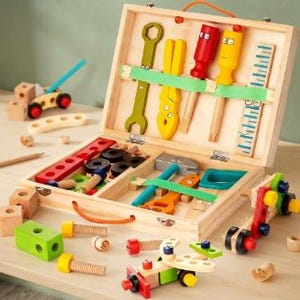 Può includere: Un set di attrezzi giocattolo in legno in una valigetta aperta, con chiave inglese, pinze, cacciaviti e un righello fissati da una cinghia verde. Il set include vari blocchi di legno, viti, bulloni e veicoli giocattolo con ruote rosse e nere.