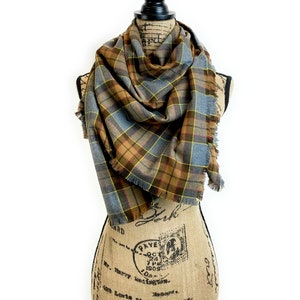 May include: A brown, yellow and blue plaid scarf with fringed edges. The scarf is draped around a fabric-covered mannequin.