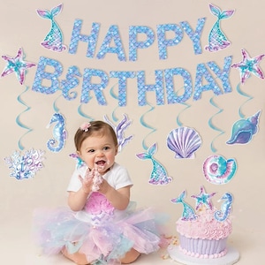 May include: A mermaid-themed birthday party decoration set featuring a blue scale-patterned banner that reads HAPPY BIRTHDAY, accompanied by hanging cutouts of seahorses, seashells, starfish, and coral, plus a matching frosted cupcake.