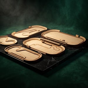 May include: A collection of four light-colored wooden race track models featuring distinct circuit layouts. Each track is enclosed within a rounded rectangular frame, showcasing intricate engraved paths and curves on a smooth, flat surface.