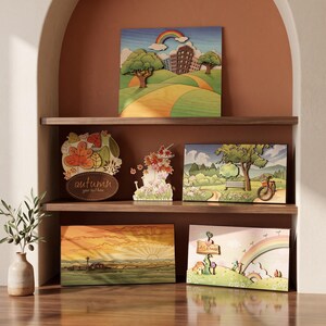 Könnte beinhalten: Eine Sammlung von fünf geschichteten Wandkunstwerken aus Holz mit verschiedenen Landschaften, darunter eine Stadt mit Regenbogen, ein herbstliches Schild mit dem Text autumn, eine Parkszene mit Fahrrad, ein Bauernhof bei Sonnenuntergang und ein Schild mit ASA house.